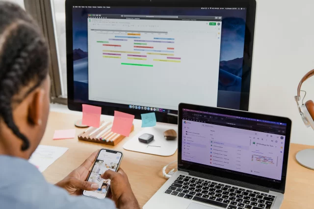 Professional managing a PR project timeline using a digital Gantt Chart on multiple screens.