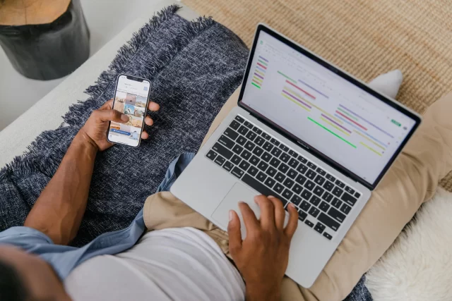 Professional using a smartphone and laptop to manage a project schedule via a Gantt Chart.