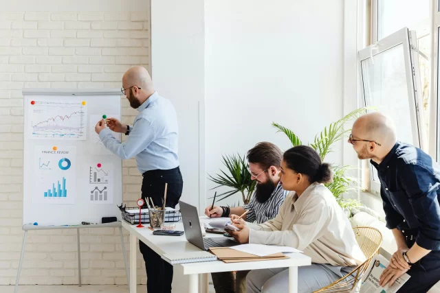 A diverse team collaborates in an office setting to refine their PMO strategy during a presentation.