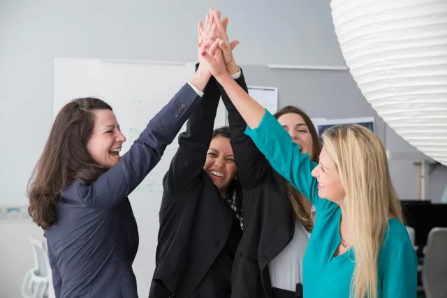 A diverse team of professionals celebrating the success of their PMO strategy with a high five.