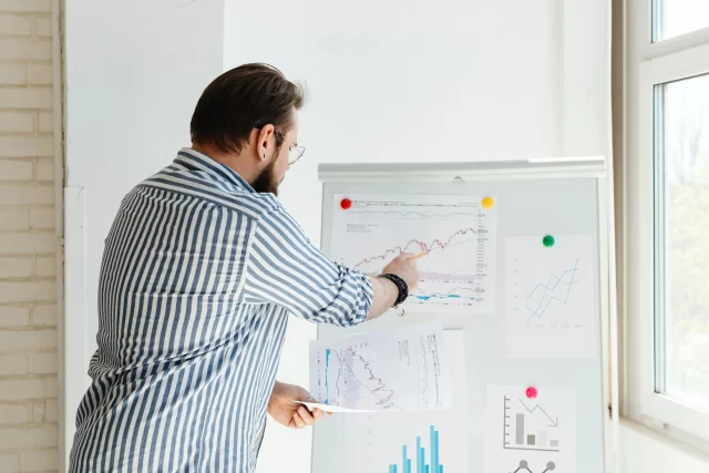 A financial analyst uses charts on a whiteboard to illustrate key strategies for Project Management in Banking.
