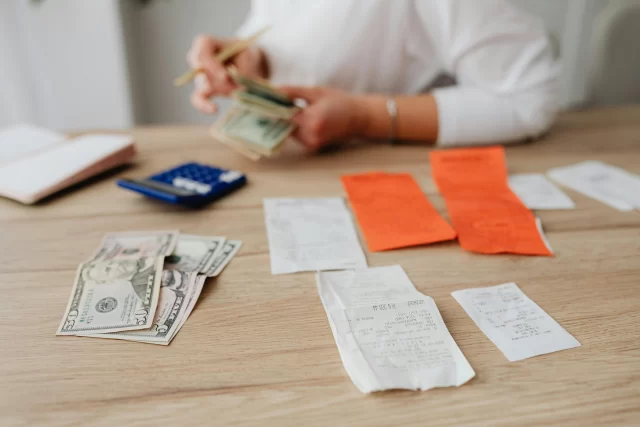 Hands sorting US dollar bills and receipts on a wooden table to demonstrate Project Budget Management.