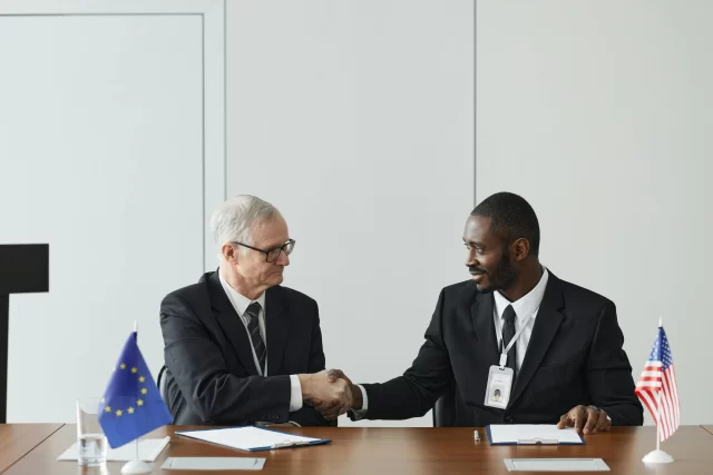 Two officials from the EU and USA shaking hands to solidify a cross-border Project Budget Management agreement.