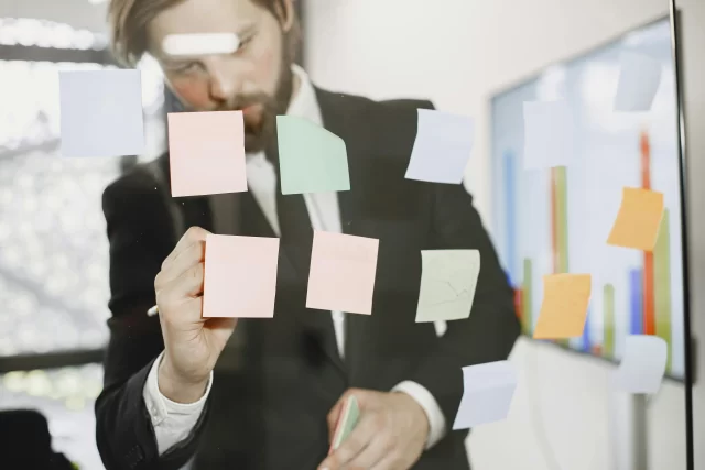 A businessman arranging sticky notes on a glass wall to define a Risk Breakdown Structure.