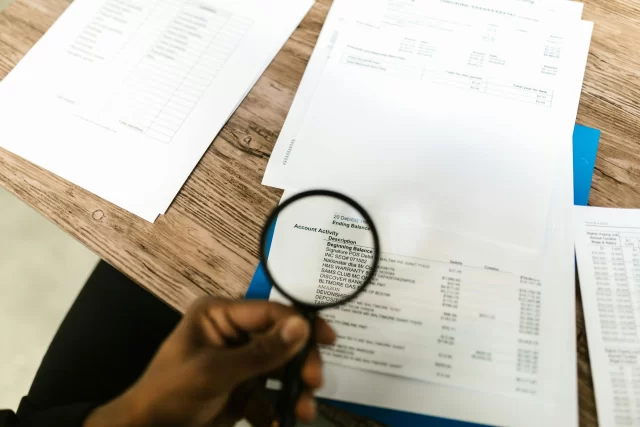 Close-up of an auditor using a magnifying glass to review B2B Auction financial statements and account activity.