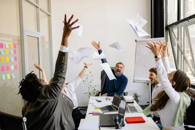 A diverse professional team celebrating the completion of a complex Task Breakdown in an office.