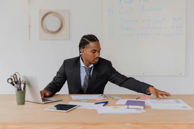A program management professional working at a desk with a laptop and documents.