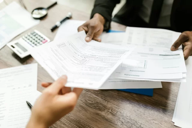 A Swiss Program Management Professional hands document forms to a colleague during a financial review session.