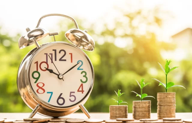 An alarm clock beside stacks of coins with growing plants, illustrating the principles of Switzerland's Lean Management.
