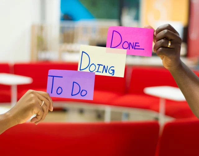 Two people hold up sticky notes labeled To Do, Doing, and Done, representing Agile in Switzerland methodology.