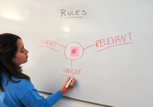 A woman writing "UNIQUE", "RELEVANT", and "RULES" on a whiteboard outlining three rules for creating a hashtag for Swiss ICE CRM.